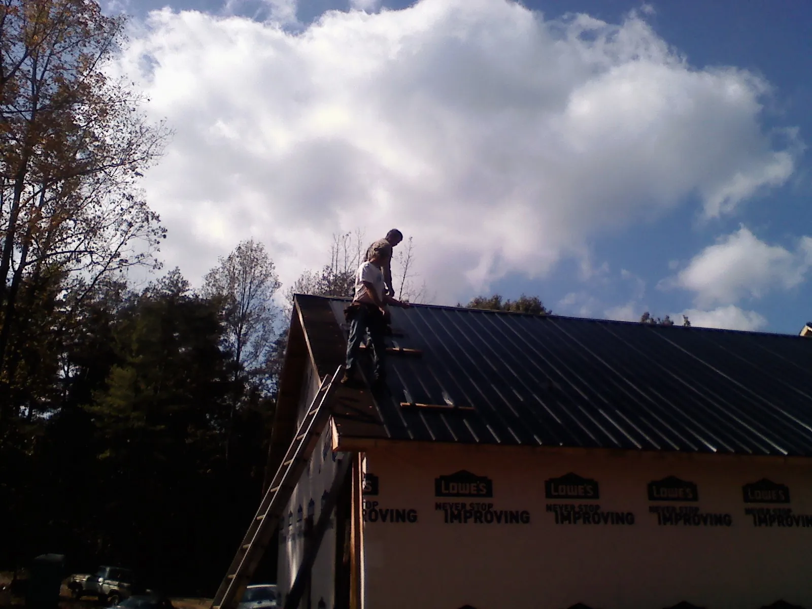 Roofer fastening dark metal panels high against a cloudy sky, from a Roof Inspection job in Atlantic