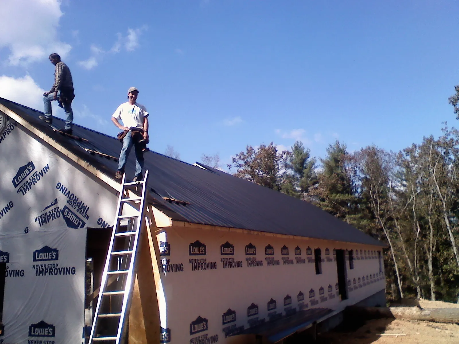 Two roofers standing on a long dark metal roof over a wrapped building in Atlantic
