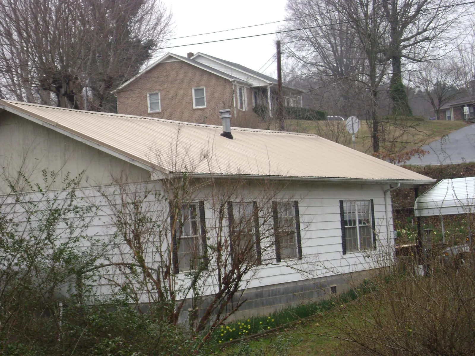Tan metal roof on a white sided house set into a hillside — Commercial Roofing by Roofing Brothers in Atlantic